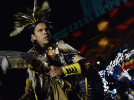 Native Peoples Day Native American dancer in feathered regalia performing at a nighttime powwow